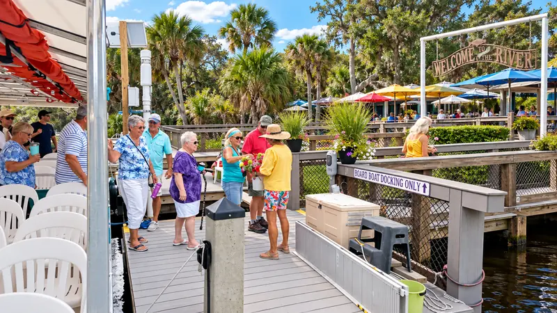 Visitors walking near the covered tour boat and riverside boardwalk